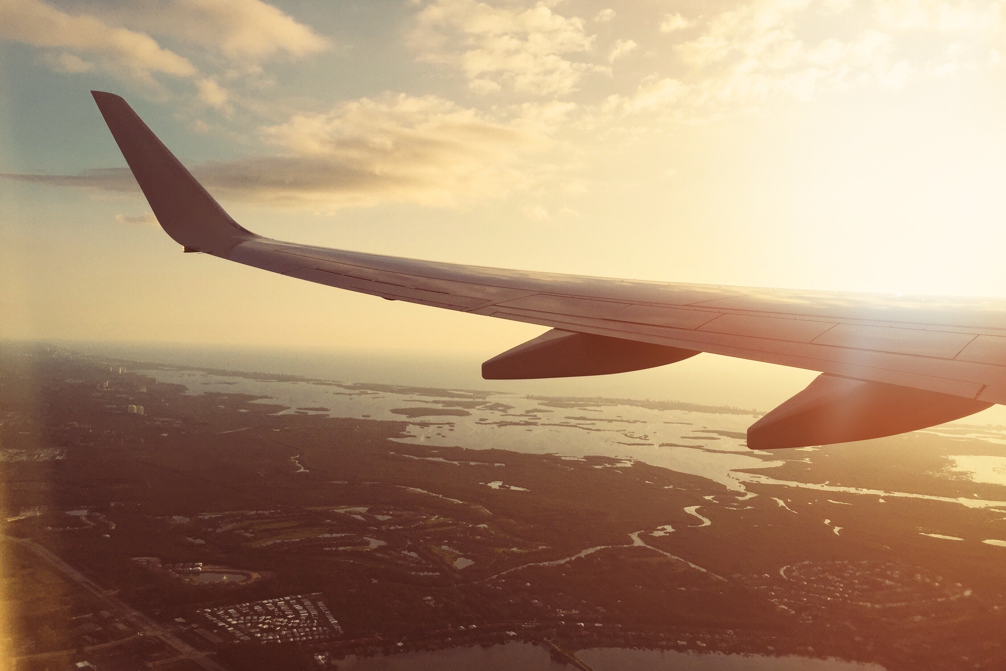 a view out of the left side of a flying plane on a sunny city with water as a banner